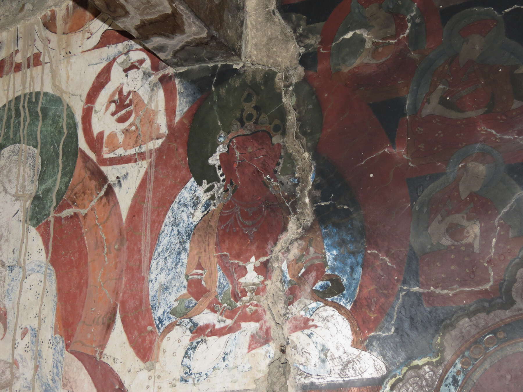 Several large cracks on deteriorated wall painting of Buddha and bodhisattvas around him.