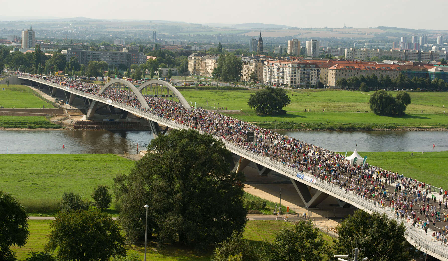 Long bridge over a river and field completely filled with crowds of people as they head toward the city in the background.