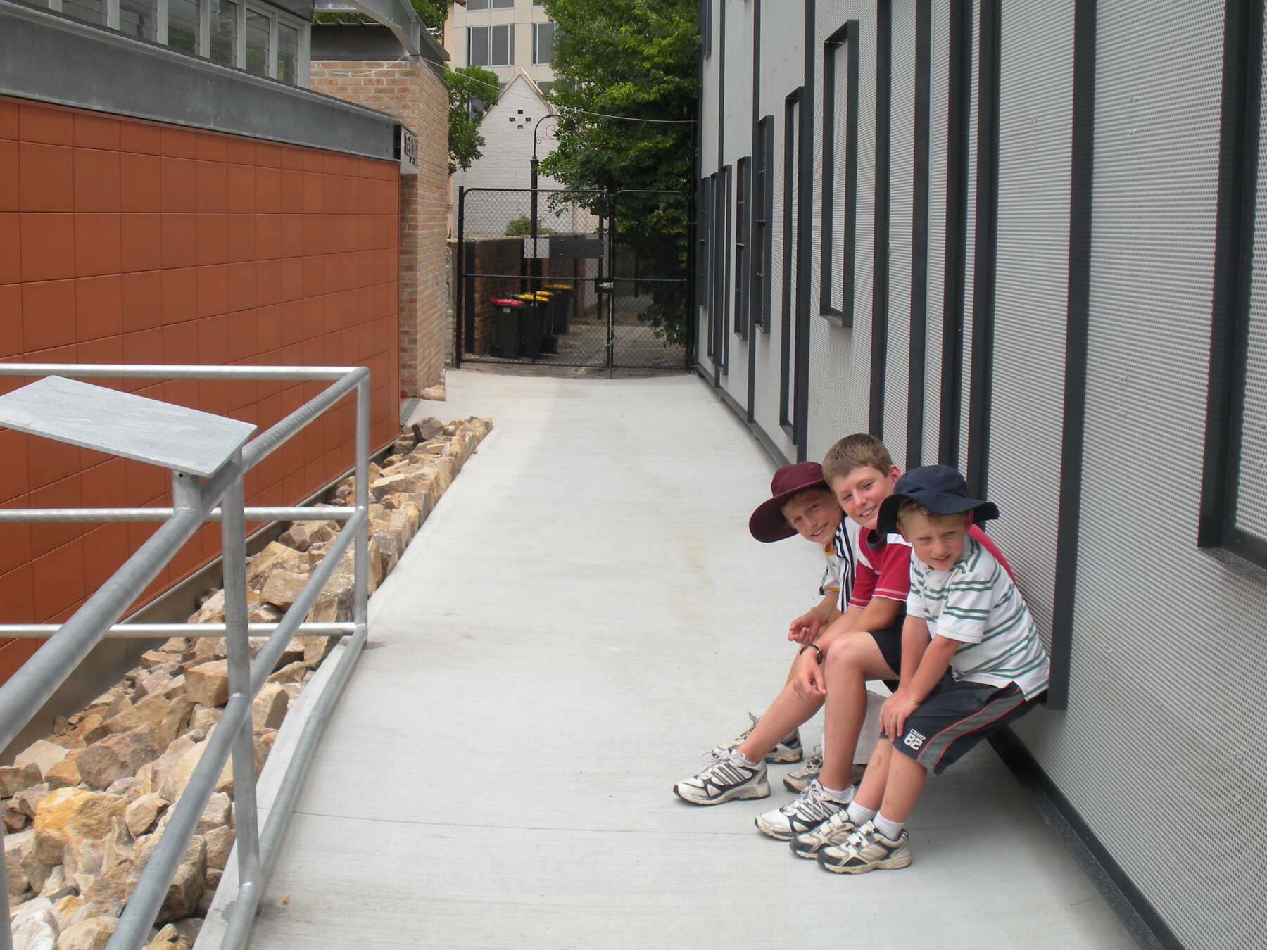 View of a small lane with new modern buildings all around and on the right, three boys lean against a wall.