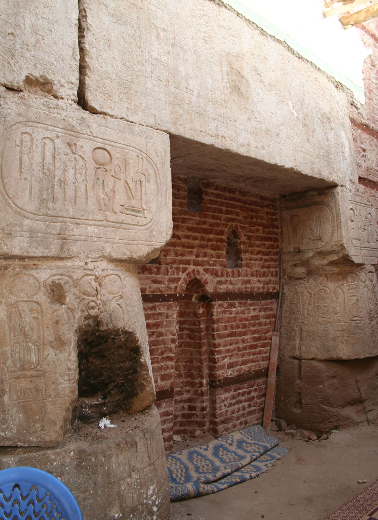 Mosque interior, focus on a brick feature wall with a niche. Around it are large sandstone blocks engraved with hieroglyphs.
